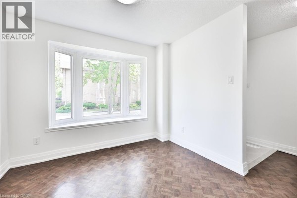 Living area with white walls, dark parquet flooring, and a large bay window. - 4635 Regents Terrace Unit# 2, Mississauga