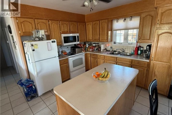 Kitchen with oak cabinets, white appliances, an island, and tiled flooring. - 464 Route 255, Saint Andre