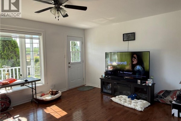 Living room with hardwood floors, a large television, windows, and a door to the outside. - 464 Route 255, Saint Andre