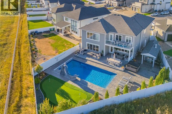 Aerial view of a backyard with a blue swimming pool, hot tub, patio furniture, and a putting green. - 464 Woolf Bend, Saskatoon