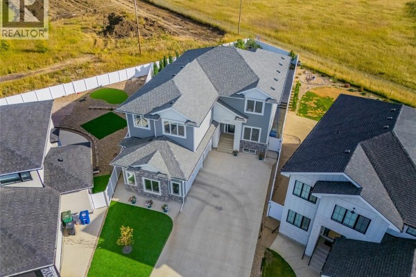 Aerial view of a large, modern grey house with a triple car garage and neatly landscaped front yard. - 464 Woolf Bend, Saskatoon