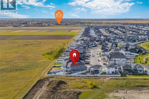 Aerial view showing the location of the house within a new suburban neighborhood and surrounding open fields. - 464 Woolf Bend, Saskatoon
