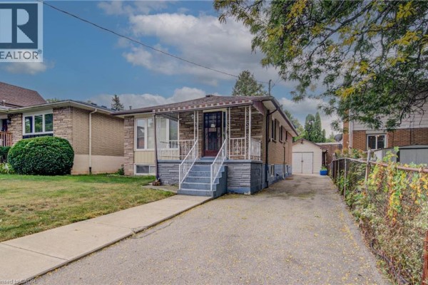 Side view of the detached bungalow showing a long driveway, chain-link fence, and garage at the rear. - 465 Herkimer Street, Hamilton
