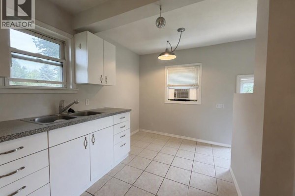 Kitchenette area with white cabinets, granite countertop, double sink, and a window. - 4653 55th Avenue, High Prairie