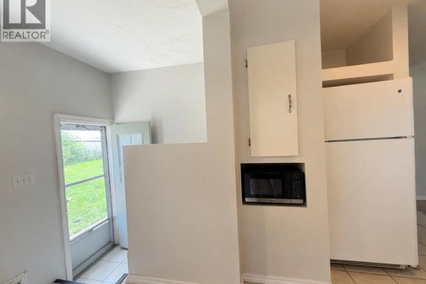 Kitchen with a refrigerator, microwave, white cabinets, and a back door to the yard. - 4653 55th Avenue, High Prairie