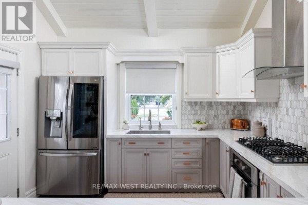 Renovated kitchen with stainless steel fridge, gas range, marble counters, mosaic backsplash & exposed beams - 4653 Dundas Street W Toronto