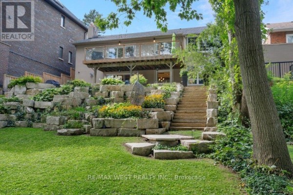 Tiered backyard with stone walls, gardens, stone stairs, and deck - 4653 Dundas Street W Toronto