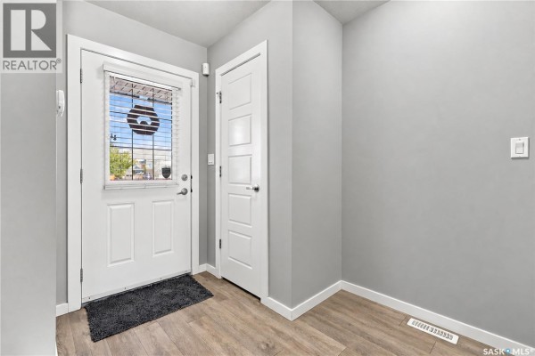 Living room with grey sectional sofa, white cabinet, and wood laminate flooring. - 4653 Primrose Green Drive E, Regina