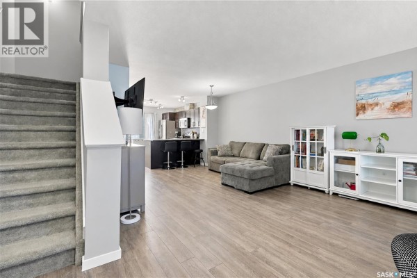 Open concept living area with kitchen island, bar stools, and view to back door. - 4653 Primrose Green Drive E, Regina