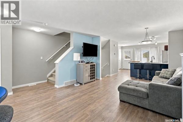 Staircase landing and living room area with light grey walls and light wood flooring. - 4653 Primrose Green Drive E, Regina