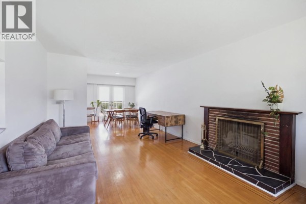 Living room with a grey sofa, brick fireplace, and hardwood floors. - 4656 Brentlawn Drive, Burnaby
