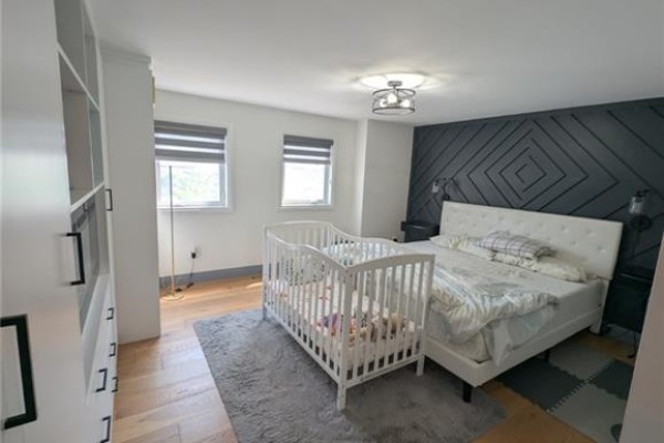 Bedroom with a grey upholstered bed, plaid bedding, a white nightstand with a lamp, and a small window. - 466 Bankside Drive, Kitchener