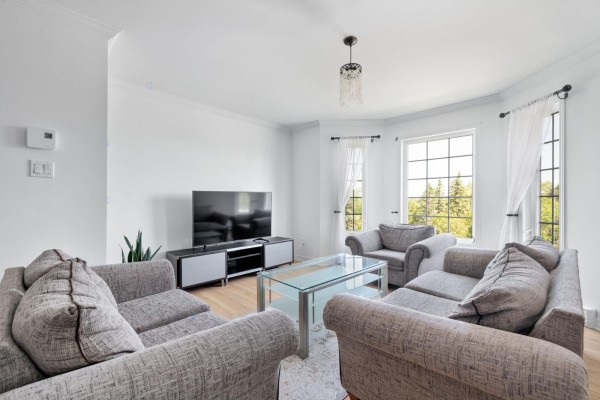 Living room with gray sofas, glass coffee table, television, and large bay window with white curtains. - 467 Rue De Cannes, Gatineau