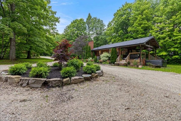 Gravel driveway leading to a bungalow nestled amongst trees. Sign reads 467042. - 467042 12th Conc B Concession, Grey Highlands