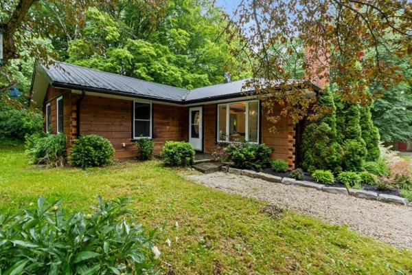 View of the bungalow's covered back porch with a hot tub, surrounded by landscaping. - 467042 12th Conc B Concession, Grey Highlands