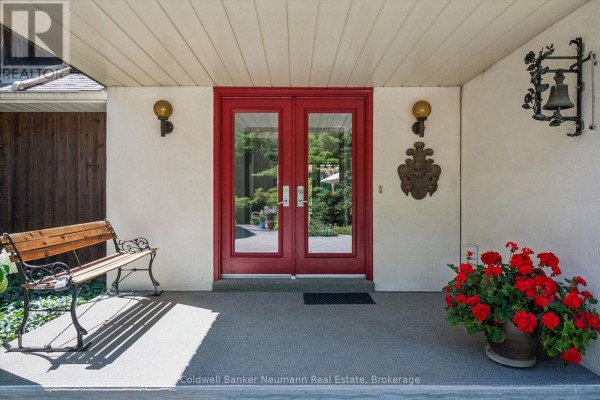Front entrance of the house featuring red double doors, a wooden bench, and potted red flowers. - 4676 Concession 11 Road, Puslinch