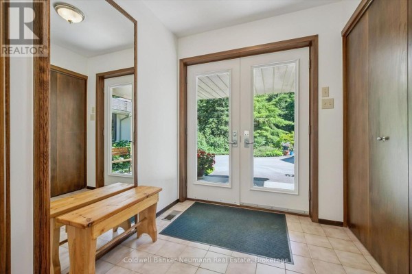 Interior entryway with light beige tiled floor, a wooden bench, a large mirror, and double glass doors. - 4676 Concession 11 Road, Puslinch