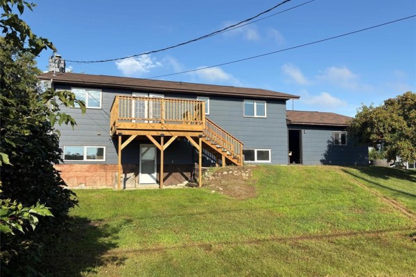 Rear view of a dark blue house with a wooden deck and stairs leading to the backyard. - 468 4th Street Ne, Minnedosa