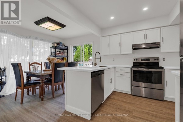 Kitchen island with sink, dining area with wooden table and chairs, and stainless steel stove. - 468 Grove Street E, Barrie