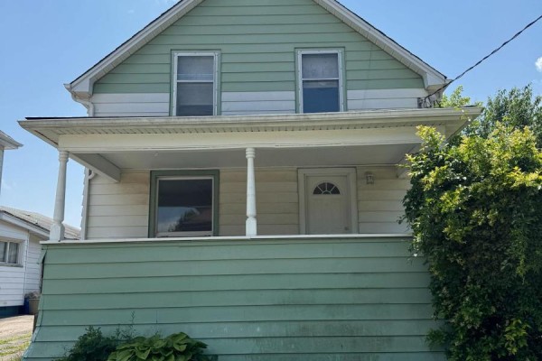 Front exterior of a residential house with green and white horizontal siding and a covered porch with white posts. - 4680 Ryerson Crescent, Niagara Falls