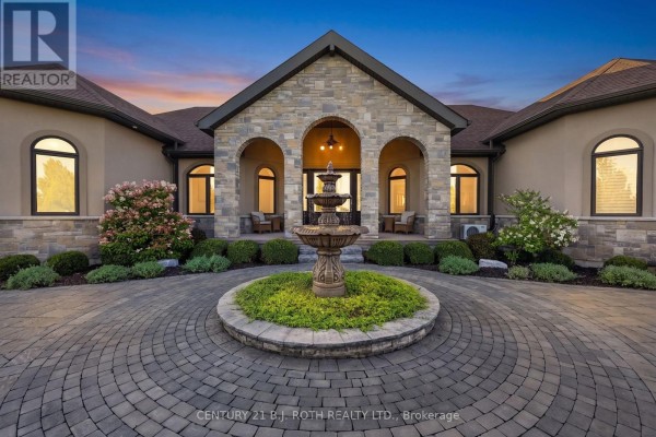 The front entrance of a stone-clad house with a circular driveway and a tiered fountain. - 4688 5th Side Road, Essa