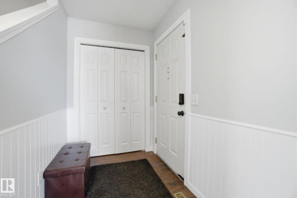 Interior entryway with a white door, two white bi-fold closet doors, and a brown storage bench. - 469 Cranberry Wy, Sherwood Park