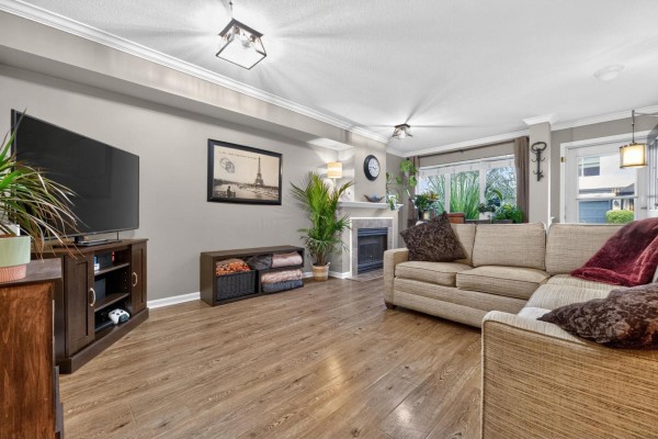 Living room with a large sectional sofa, television, fireplace, and wood-look flooring. - 47 18883 65 Street, Surrey