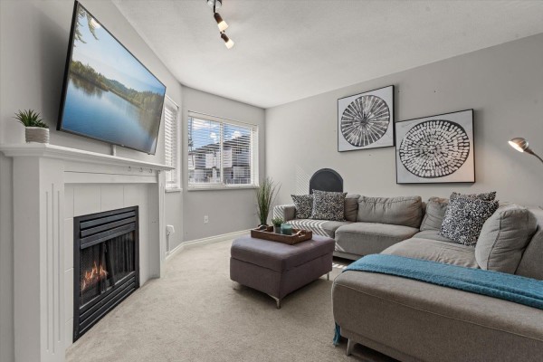 Living room with a gray sectional sofa, fireplace, and mounted television. - 47 5950 Vedder Road, Vedder Crossing, Chilliwack