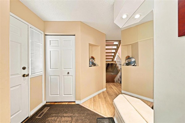 Interior entryway with a white door, closet, mirrored wall, and wooden flooring leading to stairs. - 47 Abington Road, Winnipeg