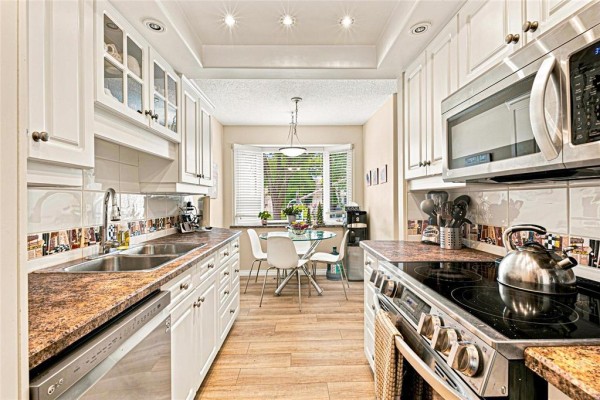 View down a galley kitchen featuring white cabinets, granite countertops, stainless steel appliances, and a dining area. - 47 Abington Road, Winnipeg