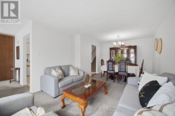 Living and dining room area with gray sofas, a dining table with chairs, and a china cabinet. - 47 Ashford Court, Brampton