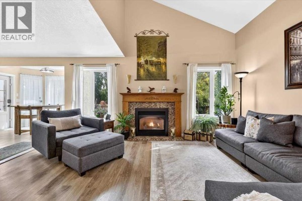 Living room with a gas fireplace, vaulted ceiling, and light wood floors. - 47 Cimarron Hill, Okotoks