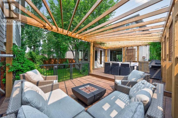 Wood deck with sectional outdoor furniture, a fire pit, and a dining set under a wooden pergola. - 47 Elgin Meadows Road Se, Calgary