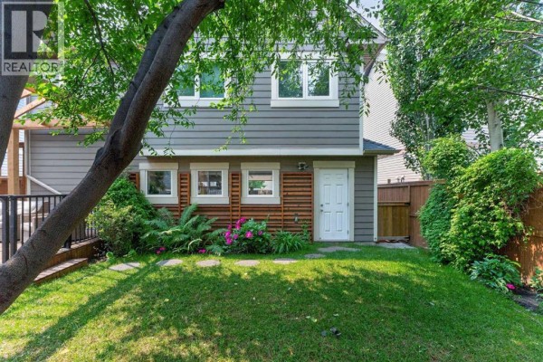 Backyard view of a grey vinyl-sided house with a white door and a small green lawn. - 47 Elgin Meadows Road Se, Calgary