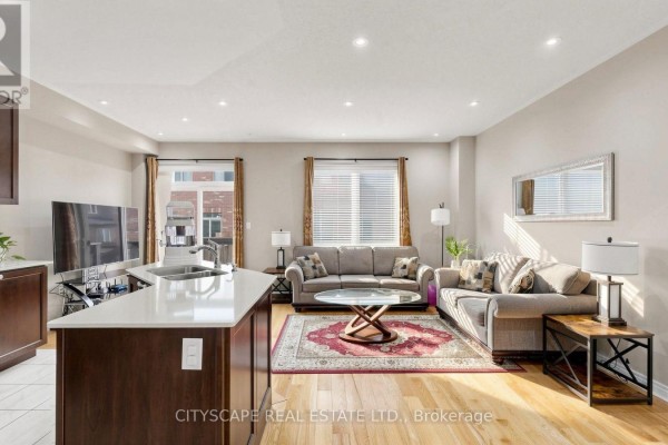 Living room with two sofas, a coffee table, and a kitchen island with pendant lights. - 47 Goodsway Trail, Brampton