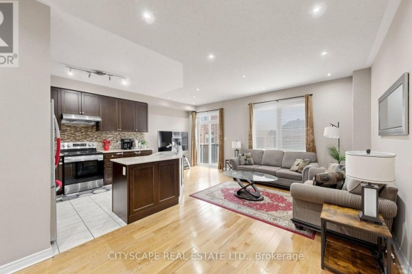 Open-concept living and kitchen area with dark wood cabinets, stainless steel appliances, and hardwood floors. - 47 Goodsway Trail, Brampton
