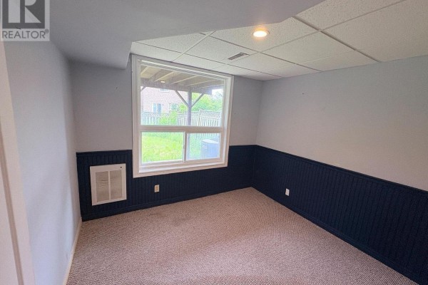 Basement room with carpet, dark blue paneled wainscoting, and a window overlooking the backyard. - Bsmt - 47 Hewitt Crescent, Ajax