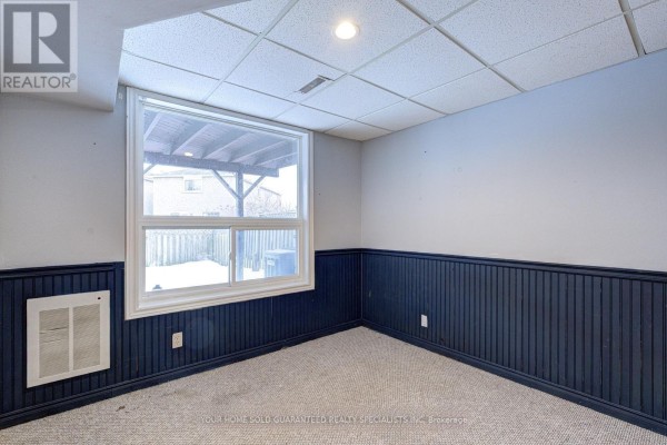 Basement room with carpet, dark blue paneled wainscoting, and a large window with a view of the backyard. - Bsmt - 47 Hewitt Crescent, Ajax