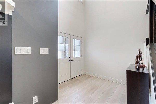 Foyer with white double doors, light wood floors, and grey accent wall. - 47 Hull Wynd, Spruce Grove