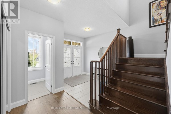 Interior view of a foyer with a dark wood staircase, double glass doors, and a hallway. - 47 Larry Crescent, Haldimand