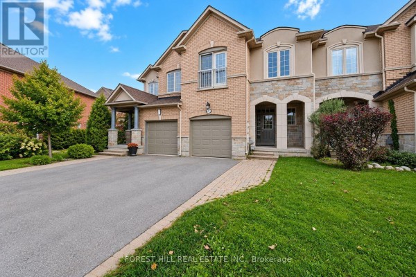 Front exterior of a townhouse with a light brick facade, stone accents, and two garage doors. - 47 Loire Valley Avenue, Vaughan