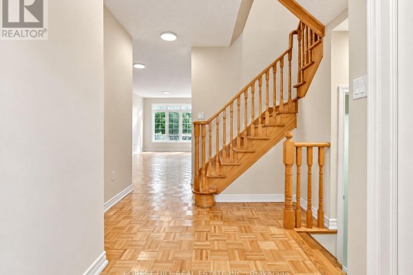 Interior hallway with light beige walls, parquet flooring, and a wooden staircase leading upstairs. - 47 Loire Valley Avenue, Vaughan