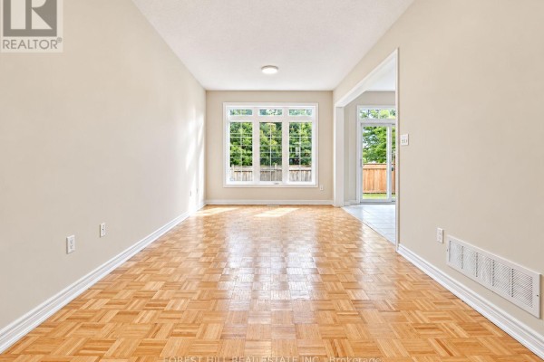 Empty living room with parquet flooring, beige walls, and a large window overlooking trees. - 47 Loire Valley Avenue, Vaughan