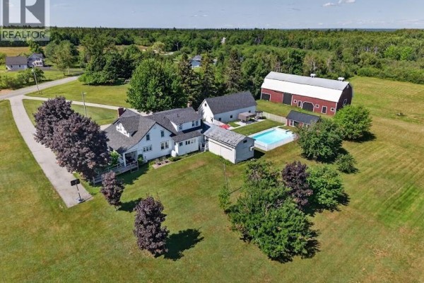 Aerial view of a white house, red barn, swimming pool, and surrounding green lawns. - 47 Nowlanville Road, Miramichi