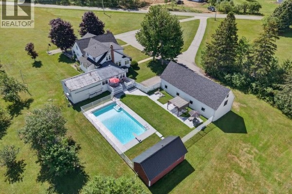 Aerial view of the property, showing the house, pool, fenced yard, and a long barn. - 47 Nowlanville Road, Miramichi