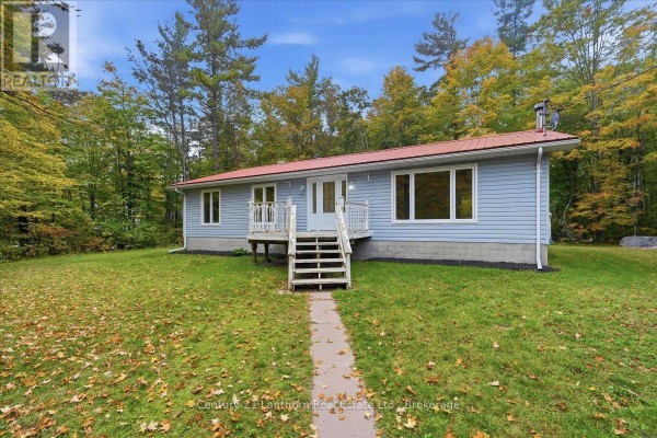 Front exterior of a light blue house with white trim, a red metal roof, and a small front deck. - 47 Reynolds Road, Madoc