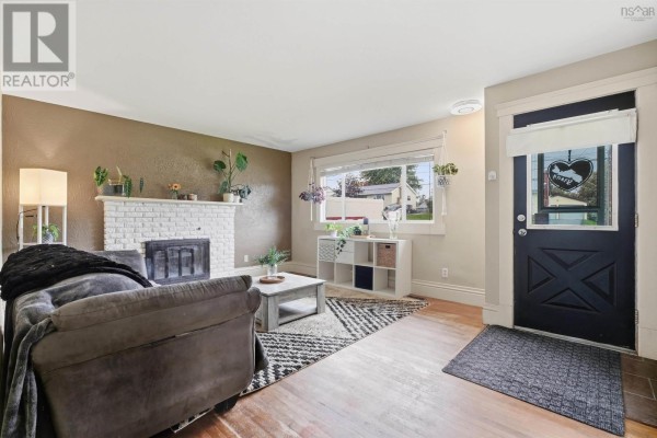 Living room with a gray sofa, white brick fireplace, and a black front door. - 47 Weyburn Road, Woodlawn