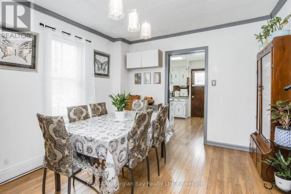 Dining room with a table set for eight, wood floors, white walls, and a doorway to the kitchen. - 470 Manly Street, Midland
