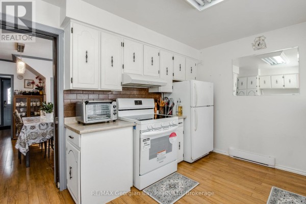 White cabinets, stove, and refrigerator in a kitchen with a toaster oven and view to dining room - 470 Manly Street Midland