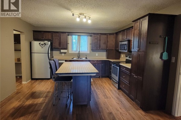 Kitchen with dark wood cabinets, island with seating, and stainless steel appliances. - 4705 Tribune Street, Macklin